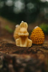 Handmade candles from natural beeswax in the shape of a rabbit,  pine cones on an old stump in the forest. Hobby. Artistic photo of beekeeping products against the backdrop of nature