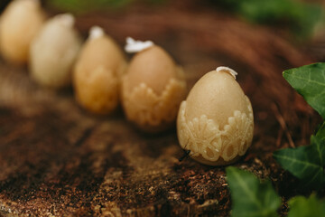 Handmade candles from natural beeswax in the shape of easter eggs on an old stump in the forest. Hobby. Gift or present for Easter. Artistic photo of beekeeping products against the backdrop of nature