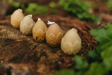 Handmade candles from natural beeswax in the shape of easter eggs on an old stump in the forest. Hobby. Gift or present for Easter. Artistic photo of beekeeping products against the backdrop of nature