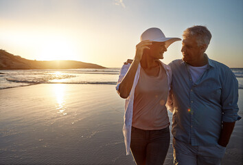 Mature, happy couple and walking with hug on beach in sunset for love, embrace or bonding in nature. Man, woman or lovers enjoying romance, support or outdoor holiday for summer, water or ocean coast