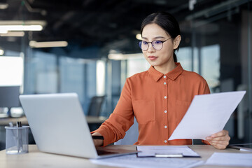 Asian financial woman working inside office with documents, papers behind paperwork, serious...
