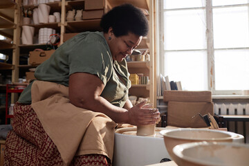 Side view portrait of smiling senior African American woman creating handmade ceramics on pottery...