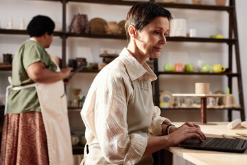 Obraz premium Side view portrait of mature woman using computer in art studio and managing small business copy space