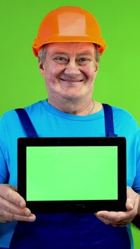 Repairman in overalls showing tablet with horizontal green screen and smiling.