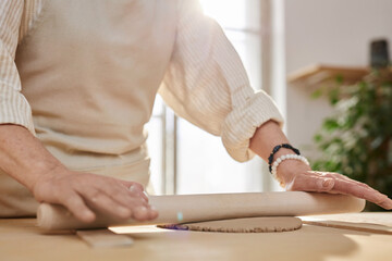 Close up of female hands rolling clay piece and creating artisanal ceramics in sunlit studio copy space