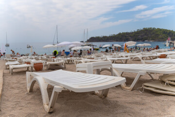 Close-up of white plastic sunbeds on the beach against the background of the blurred sea, mountains, yachts and boats.