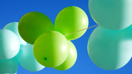 A bunch of green and turquoise balloons against blue sky