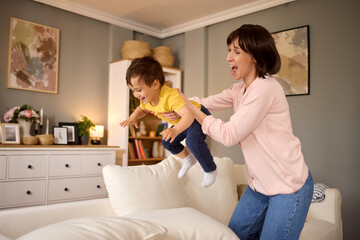 Overjoyed mother and her baby boy playing flying game in the living room