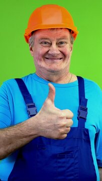 Senior worker in overalls and helmet makes perfect gesture and shows thumbs up.