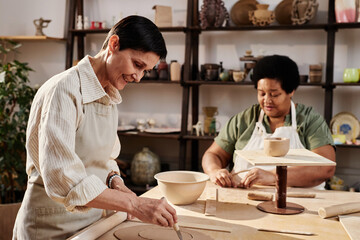 Side view portrait of smiling mature woman enjoying pottery class in sunlight copy space