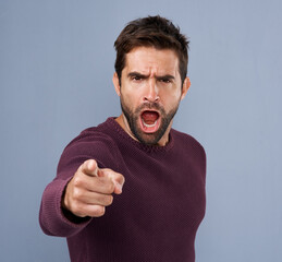 Studio, shouting and portrait of man, pointing and angry with you, choice or decision of recruitment. Blue background, yelling and hand of person, gesture and serious of opinion and finger in England
