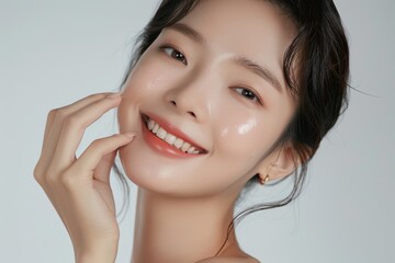 Portrait of beautiful young asian woman with clean fresh skin on white background, happy smile and hand touch face isolated over grey color backdrop. Beauty treatment concept.