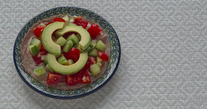 Homemade red corn tortilla topped with Pico de Gallo salsa and avocado slices on a small plate with space for text. Healthy vegan Mexican food. Table spin.