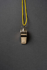 Top view of metal whistle with yellow string on dark gray background