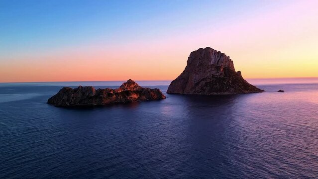 Aerial view of sun setting behind Es Vedra Ibiza during sunset. Showing ocean and clear skies.