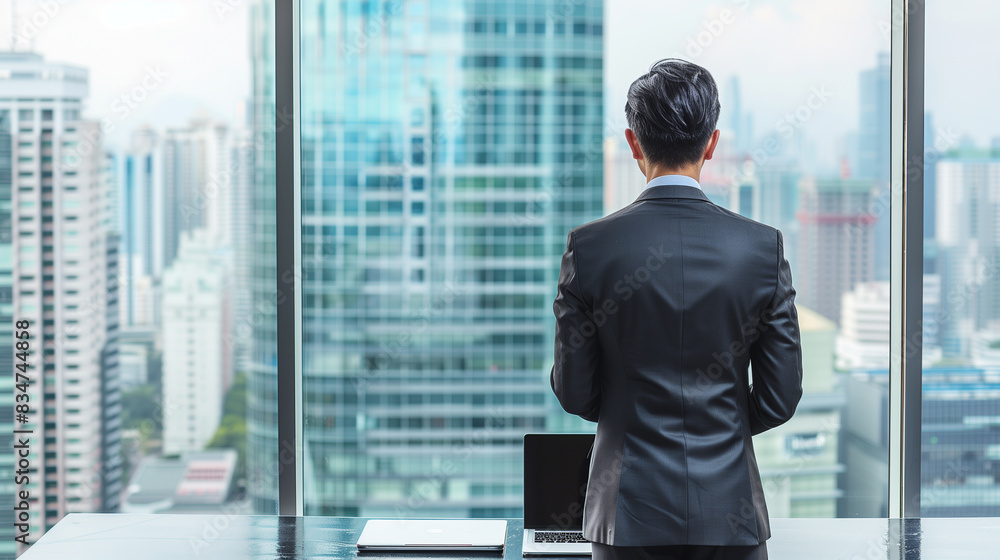 Poster a man in a suit is sitting at a desk with a laptop in front of him. he is looking out the window at 