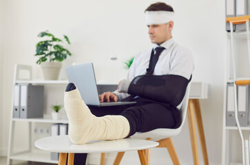 Disabled businessman with a broken leg and arm in bandage continues working in the office with a...