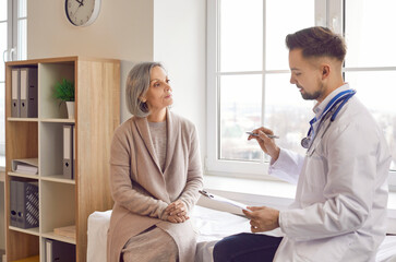 Fototapeta premium Caucasian male doctor or nurse consulting an elderly patient during a visit to the hospital office. The medical professional provides care and assistance to the senior, old individual.