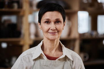 Portrait of adult Caucasian woman wearing apron and looking at camera wearing apron in pottery...