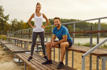 Portrait of sporty happy young couple wearing sportswear standing in city park and looking cheerful...