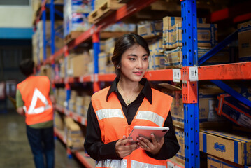 Young beauty Asian woman warehouse worker wearing safety vests checking inventory stock information...