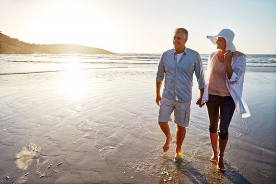 Mature, happy couple and walking with holding hands in beach sunset for love or bonding together in nature. Man, woman or lovers enjoying stroll on water for outdoor holiday or summer by ocean coast