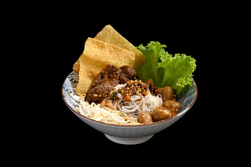 Rice noodles with sliced braised beef, meatballs and vegetables in a bowl on black background