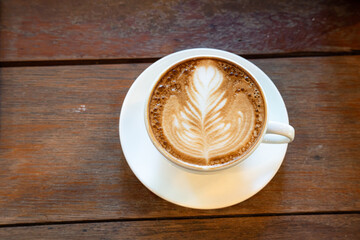 Hot coffee latte with latte art milk foam in cup mug on wood desk on top view. As breakfast In a coffee shop at the cafe,during business work concept,vintage style