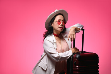 Beautiful senior woman tourist with travel bag standing on pink background. Summer, travel and...
