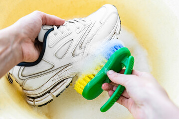 Cleaning white sneakers with a brush and detergent in a basin.