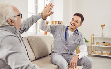 Young happy doctor physiotherapist, nurse or caregiver giving high five to a gray-haired senior...