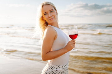 Beautiful woman at sunset with glass of wine. The girl looks at the magical sunrise. Summer time. Travel, weekend, relax and lifestyle