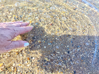 Pebbles in the water. Background, texture. Hand Disturbing Clear Water Over Colorful Pebbles