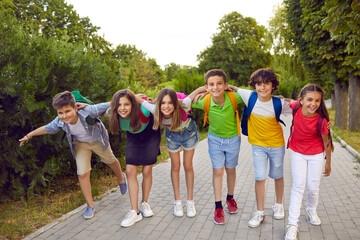 Group of friends having fun together. Six happy children playing outside after school. Several elementary students in casual clothes standing on park path, hugging, smiling and looking at camera