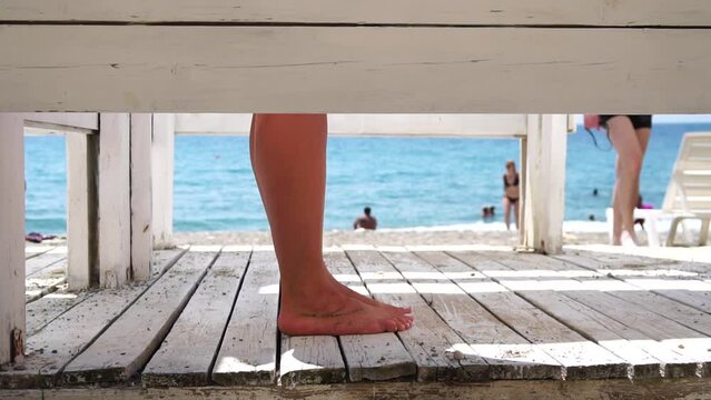 Woman in the changing, dressing room on beach, at sunset on the seashore. Close-up of bare female feet legs in enclosed changing room cabin. Summer holiday vacation and travel concept. Slow motion