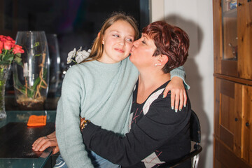 Obraz premium Positive emotions at a family holiday at home. A woman with a teenage girl on her lap gives a kiss