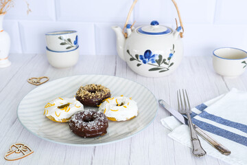 Gray plate with donuts on a white kitchen table, decorated for tea.