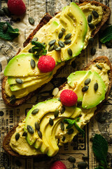 Detail of two toasts of bread with avocado, decorated with pumpkin seeds, mint and raspberry. Urban food.