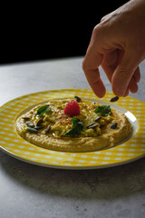 Hand sprinkling seeds on a plate of chickpea hummus.