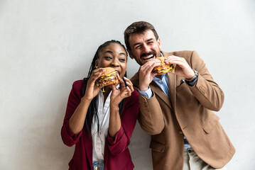Two young hipsters expatriates business people standing together eating unhealthy fast food or...