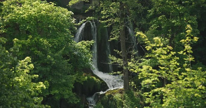 Hidden waterfall amidst dense green foliage in Rastoke, Croatia.