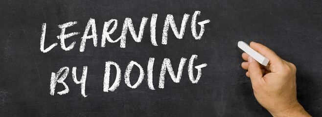  Text written on a blackboard -  Learning by doing