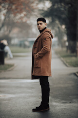 man wearing brown coat standing on sidewalk in winter park in dark weather