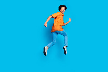 Fototapeta premium Full length photo of attractive funny guy wear orange shirt running jumping high emtpy space isolated blue color background