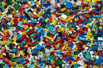 A chaotic yet colorful jumble of toy bricks, tightly packed to fill the entire frame. The bricks come in various sizes and an array of colors including red, blue, green, yellow, and white,