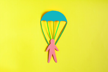 An abstract cardboard man with a colored rescue parachute in close-up.