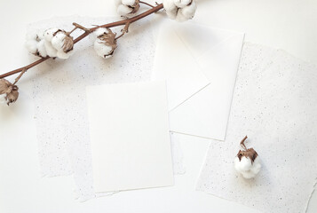 Top view of a table with blank white card and envelope and cotton plant