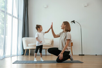 Well done, doing high five. Young woman with little girl are doing yoga at home © standret