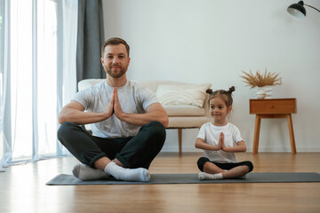 Lotus pose. Father with little daughter are doing yoga at home