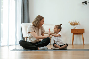 Well done, doing high five. Young woman with little girl are doing yoga at home © standret